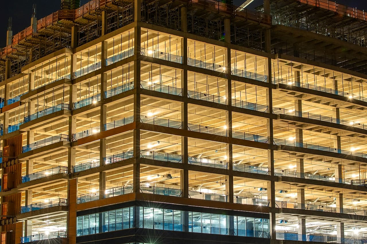 Lights illuminate an unfinished multi-storey building at night.