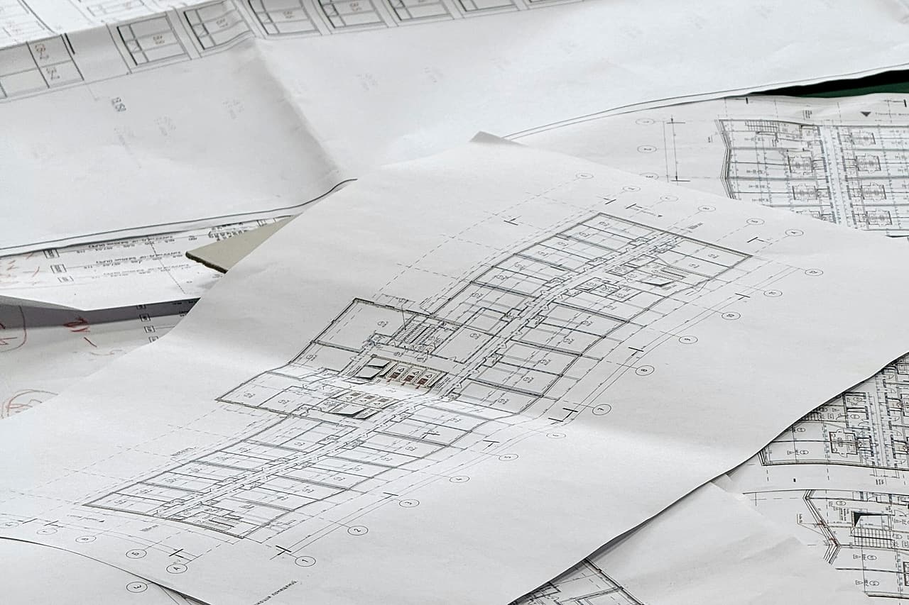 Printed floor plans spread across a table, one sheet with red handwritten markups at its edge.