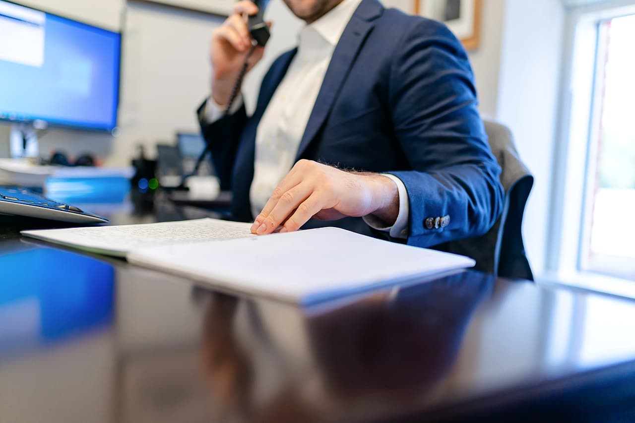 A person on a telephone call reviews papers at an office desk.
