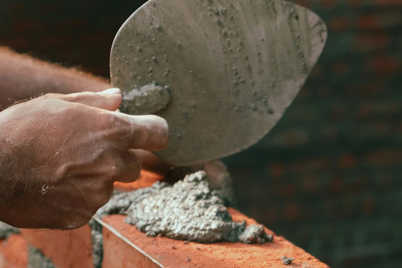 Close view of a hand spreading mortar with a trowel along a course of red bricks.