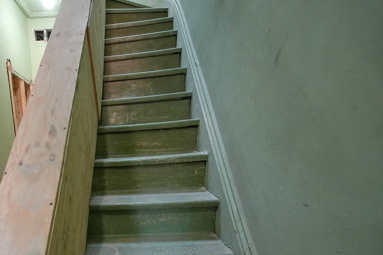 Existing timber stair beside a temporary plywood enclosure during interior renovation.