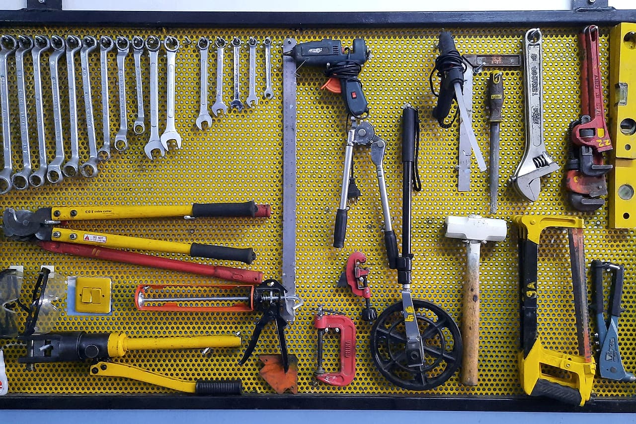 A yellow perforated tool board with wrenches, cable cutters, a caulking gun, measuring wheel, hacksaw and pipe wrench hung in place.