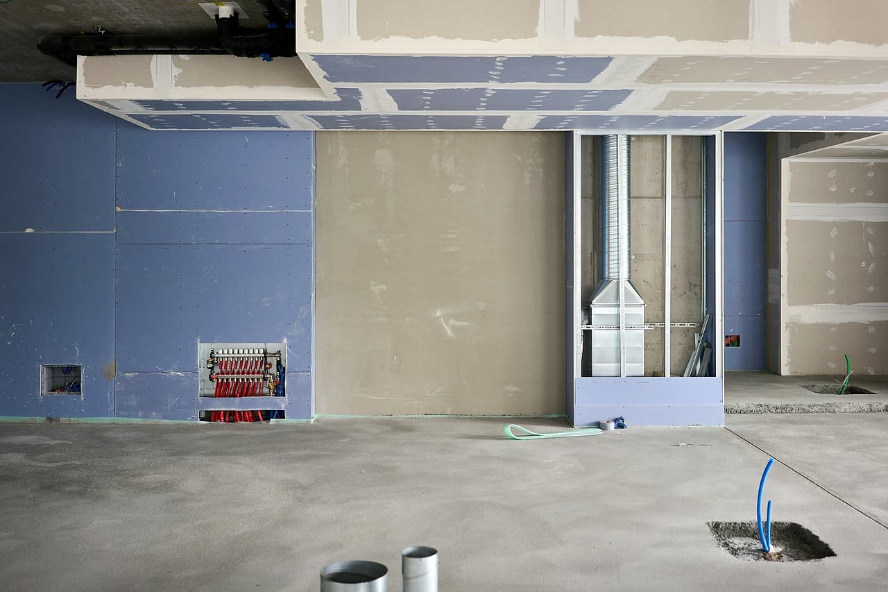 Partly installed drywall surrounds exposed services in an unfinished room.