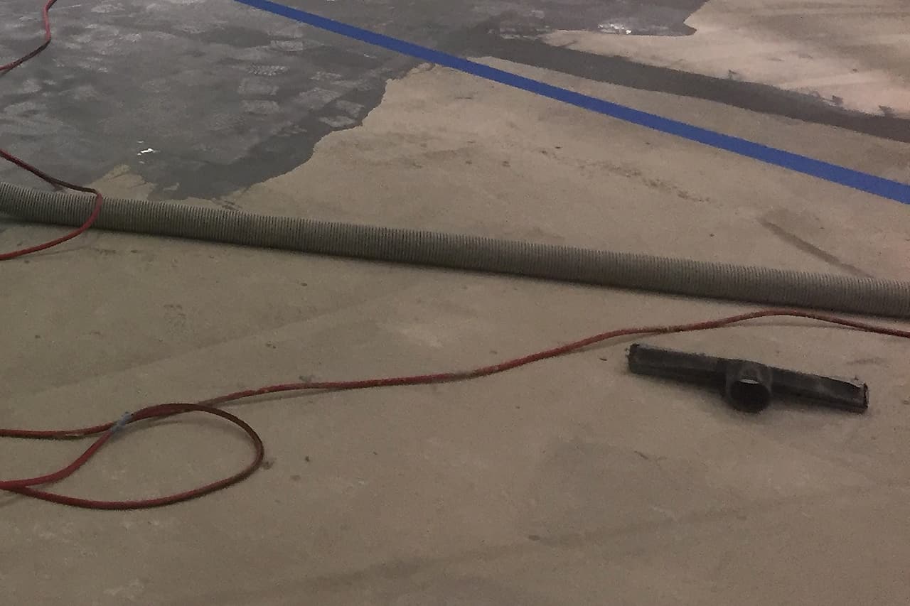 Grey repair bands cross an unoccupied concrete floor beside a vacuum hose, nozzle and red cord.
