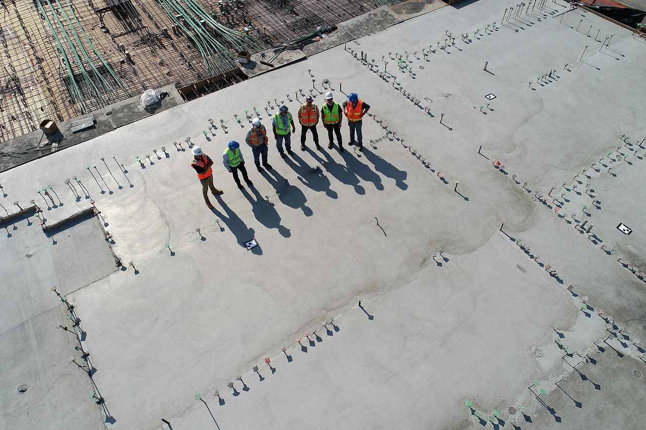 Seven workers in hard hats and reflective vests stand together on a concrete slab.