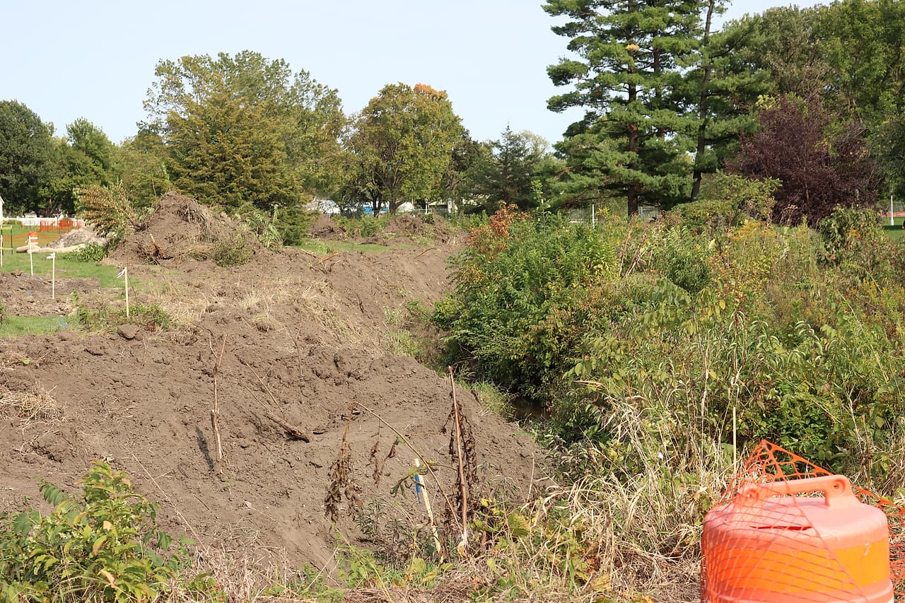 A cleared creek bank and survey markers show ground prepared for construction.