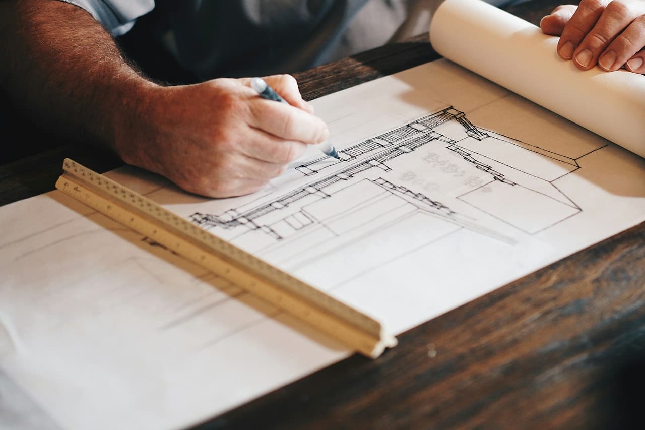 Hands mark a floor plan with a pencil beside a wooden ruler.