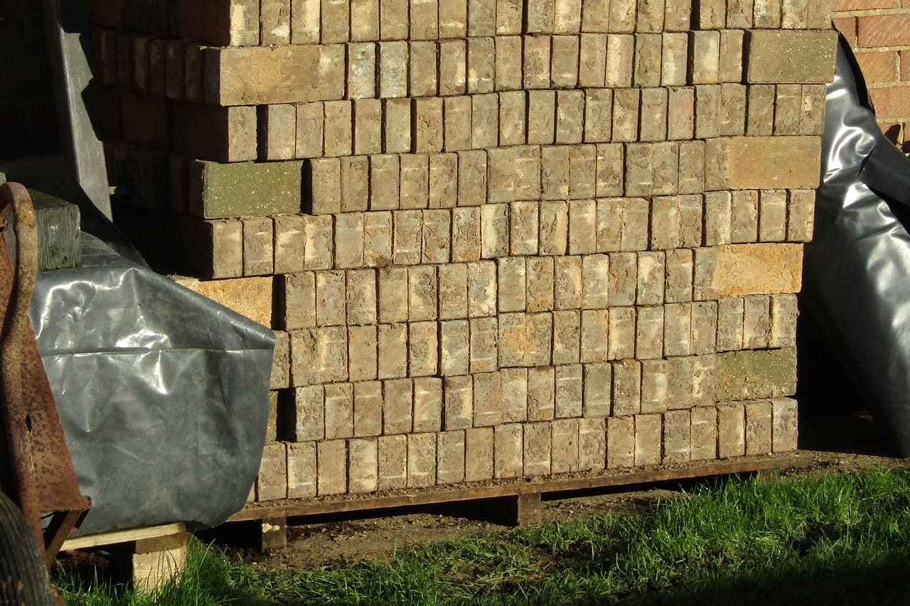 Reclaimed concrete paving blocks are stacked on a wooden pallet beside a brick wall.