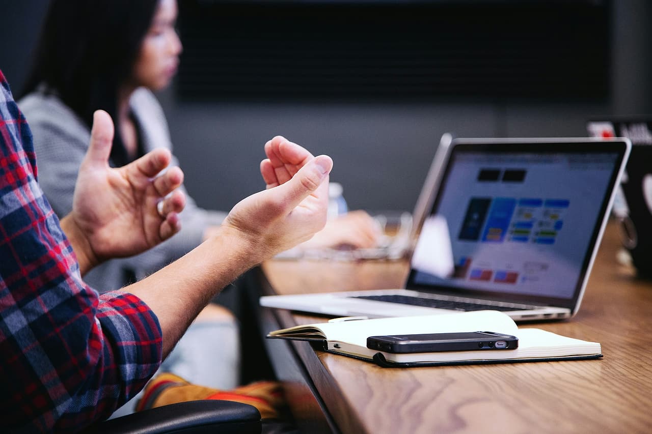 Hands gesture during a discussion beside a laptop and notebook.