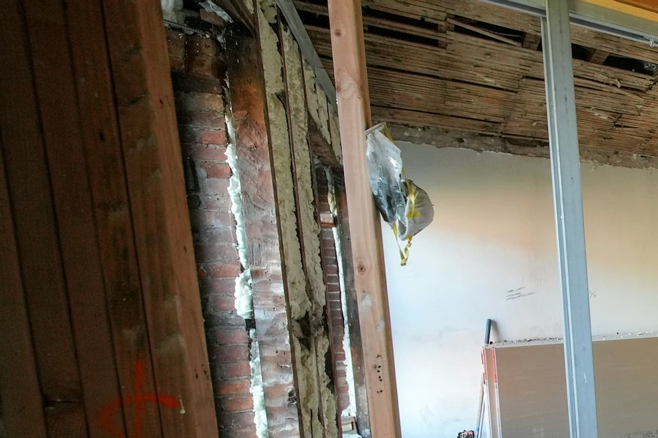 New metal partition framing beside exposed timber and brick inside a building under renovation.