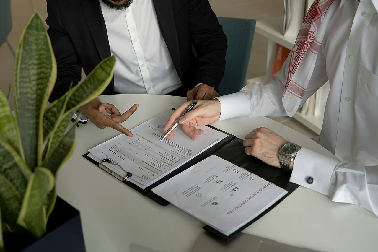 Two people at a round table go over a document on a clipboard, one pointing to a line with a pen.