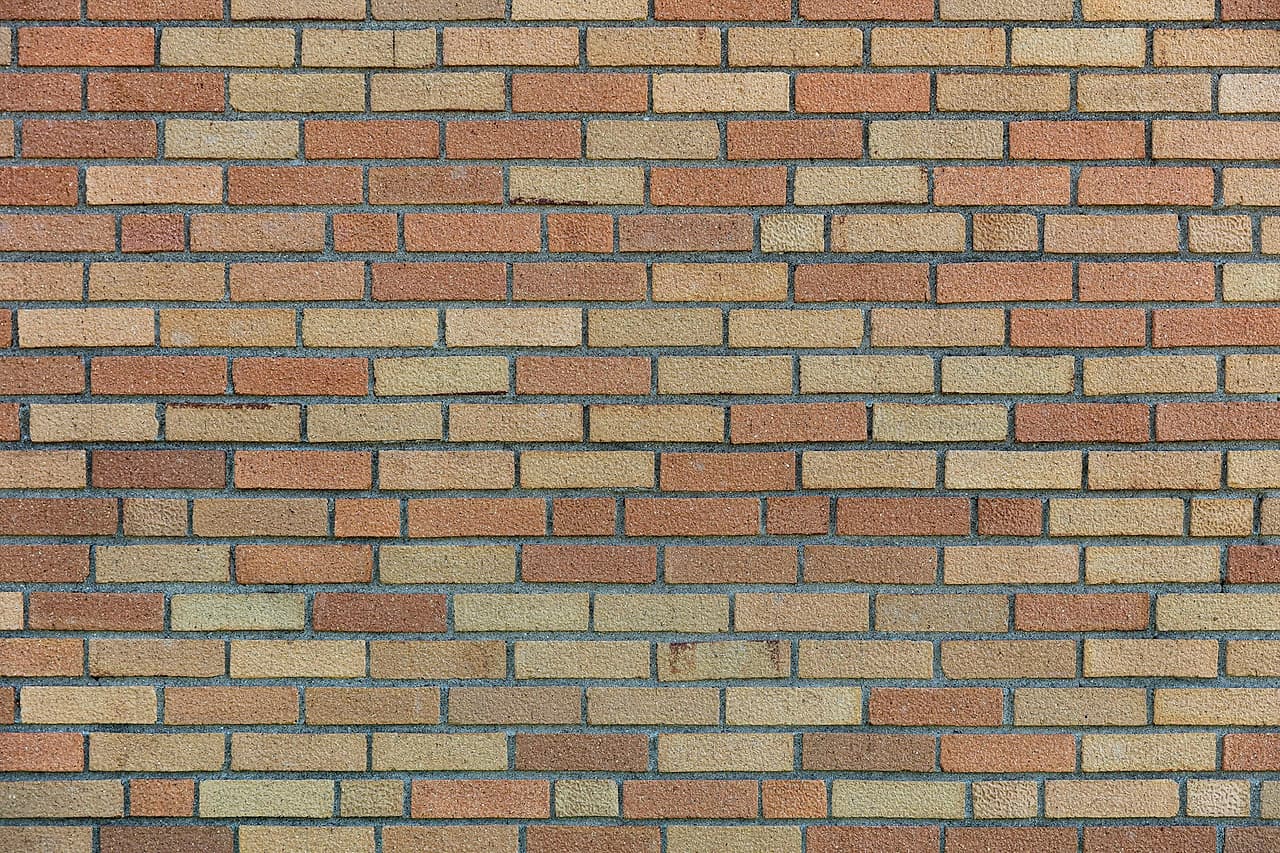 A brick wall in a blend of buff and orange bricks laid in running bond with even grey mortar joints.
