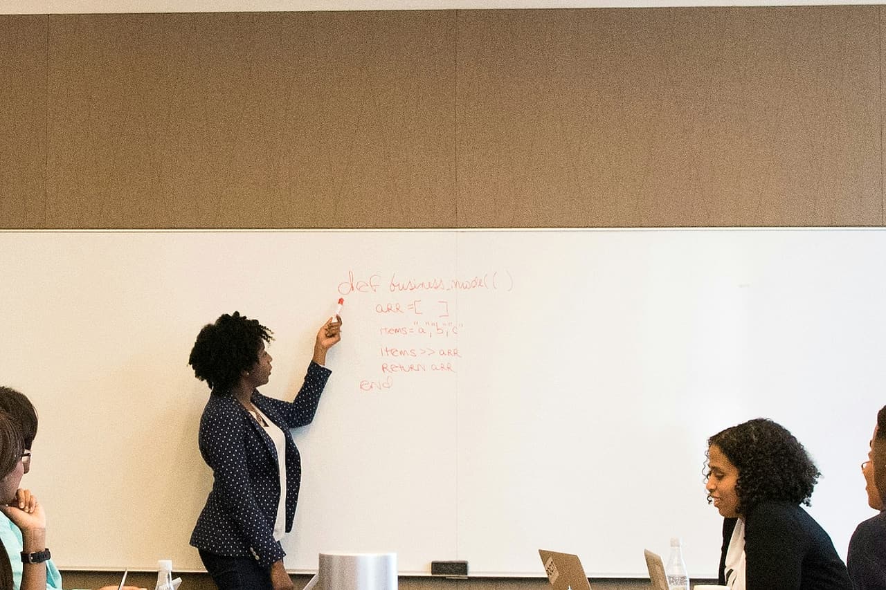 A small group listens to a colleague writing on a whiteboard.