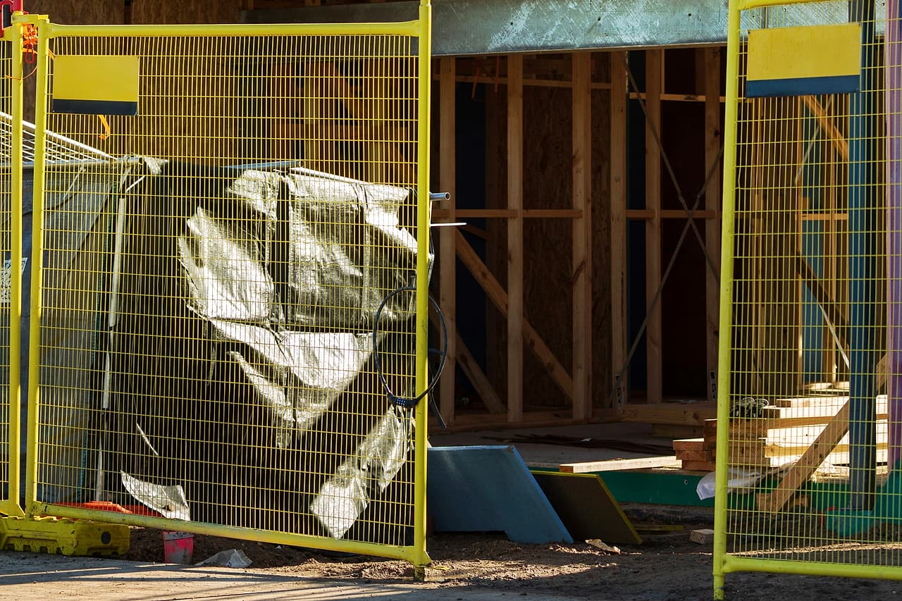A yellow mesh barrier encloses the entrance and unfinished lower level of a house under construction.