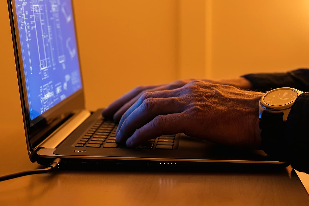 Hands type on a laptop showing a blue technical drawing, lit by warm afternoon light.