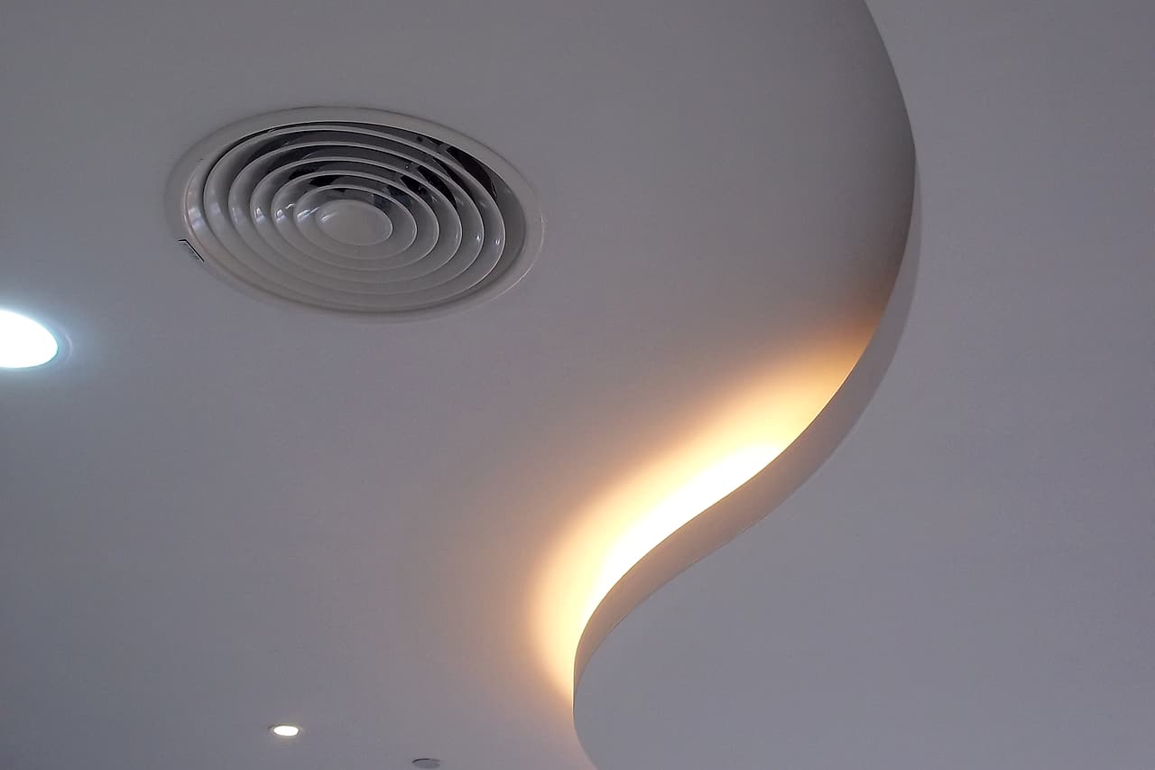 Round air diffusers and recessed lights sit within a curved ceiling.