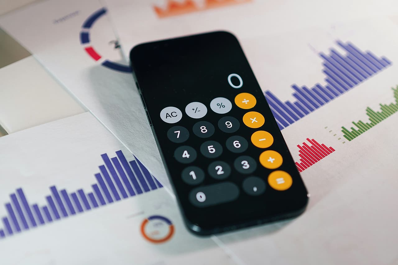 A phone showing a calculator lies across sheets of generic financial charts.