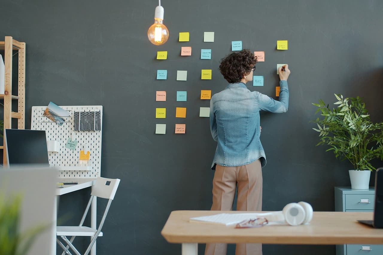 Person seen from behind arranging notes on a planning wall in an office.