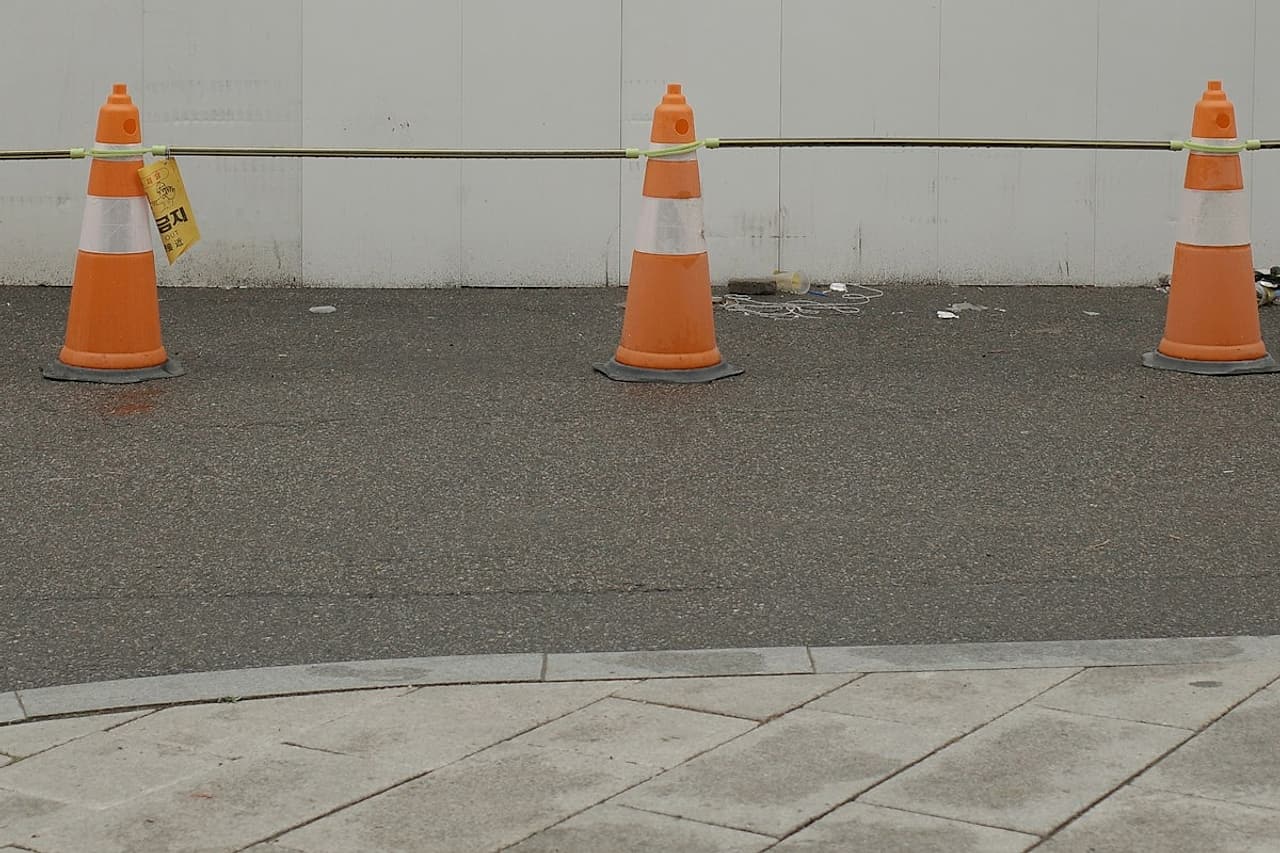 Traffic cones mark a curb lane beside construction hoarding.