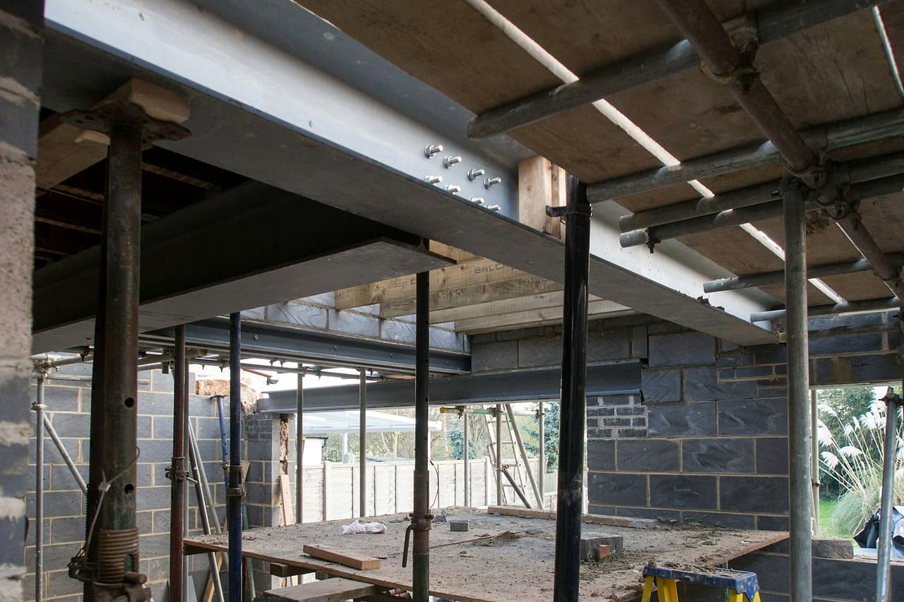 New steel beams with a bolted splice sit on temporary adjustable steel props in a house extension under construction.