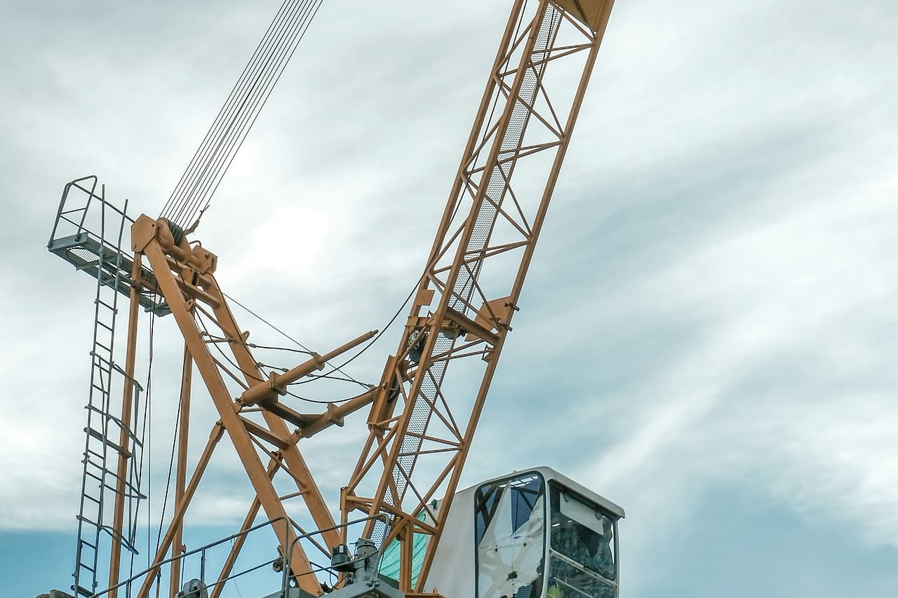 An orange tower crane cab and lattice boom stand against an overcast sky.
