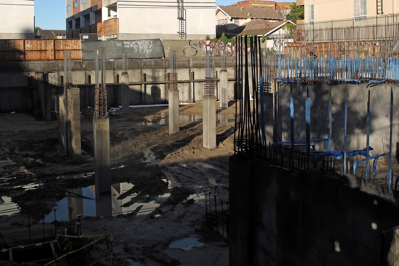 An unoccupied foundation excavation shows concrete walls, columns, reinforcing steel and puddles between the unfinished elements.