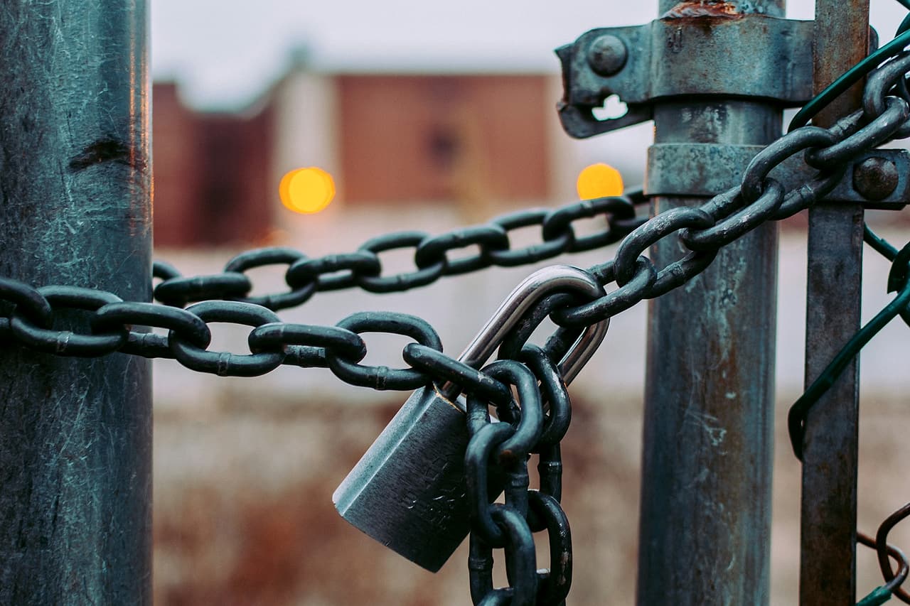 A metal padlock secures a heavy chain around two gate posts.