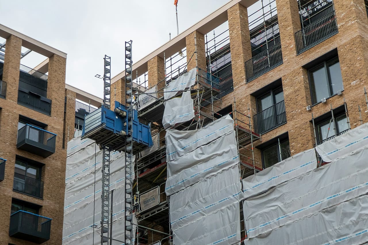 A brick apartment building, partly finished and partly wrapped in scaffold sheeting, with a construction hoist on its face.