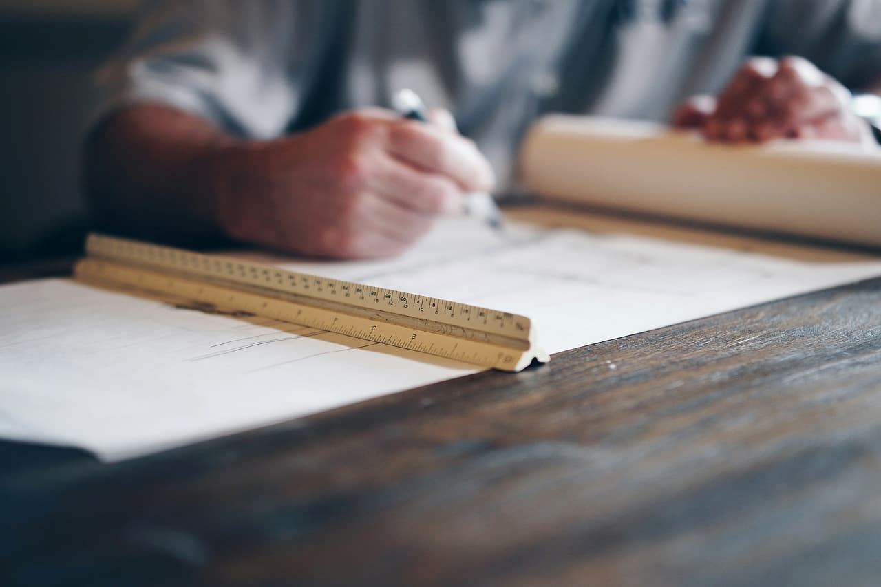 Hands draft on a drawing beside a wooden scale ruler.