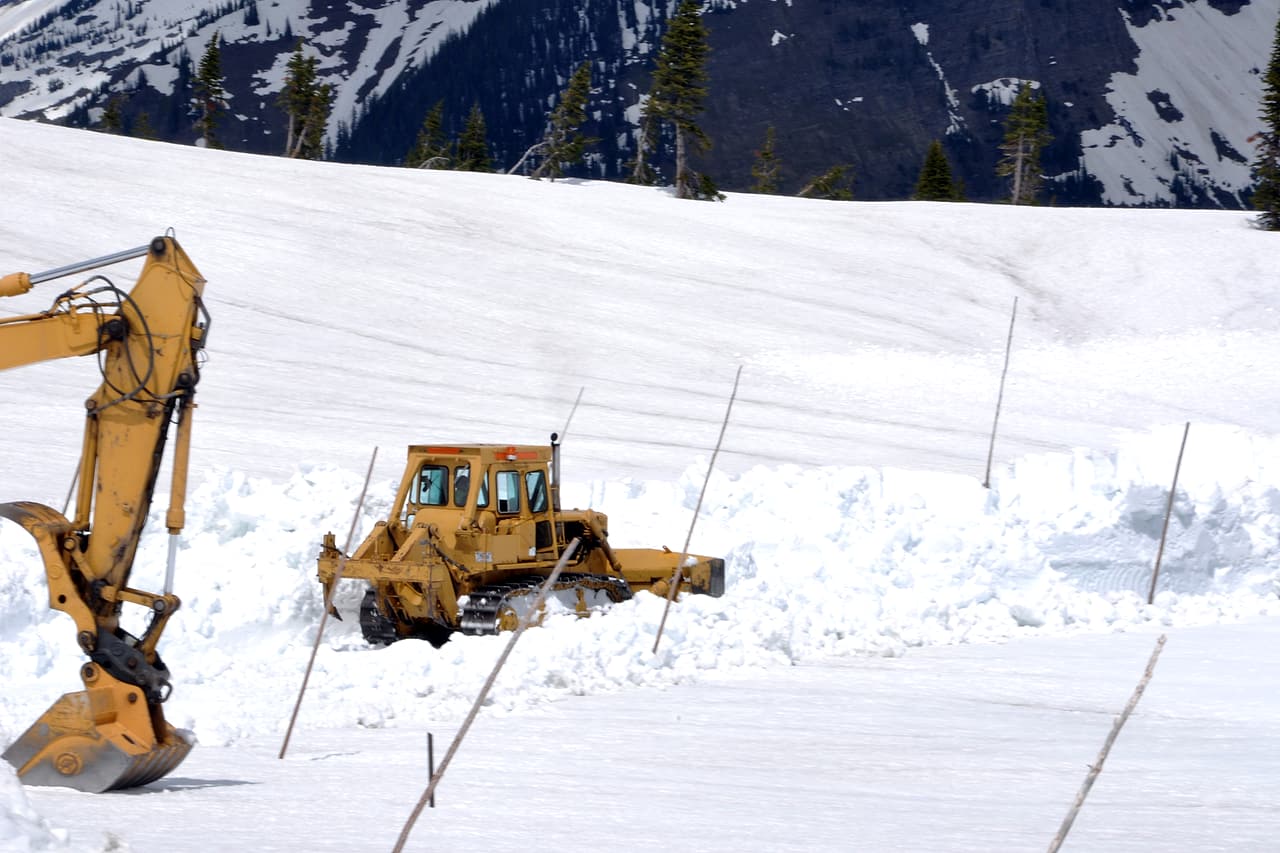 Tracked earthmoving machinery and an excavator arm are shown in a snowy mountain work area.