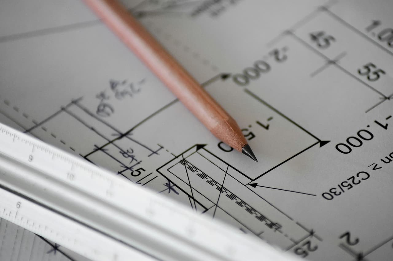A pencil points at a dimensioned detail on a structural drawing beside a scale rule.