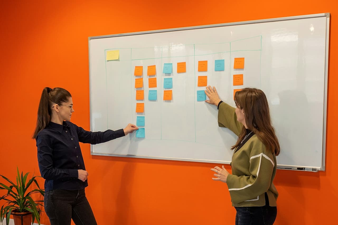 Two colleagues discuss coloured notes on a whiteboard.