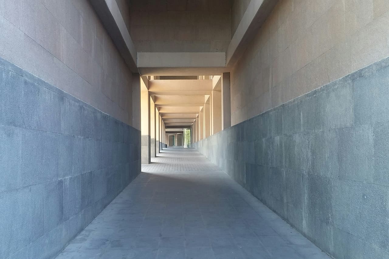 A clear concrete corridor with two-tone block walls extends through a series of open bays.