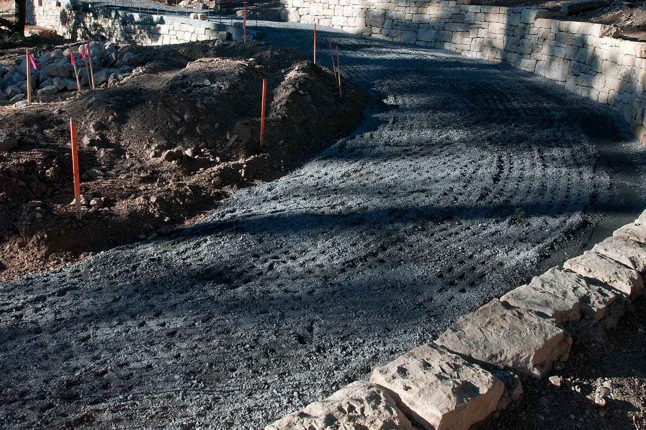 A gravel path curves between stone walls inside an unoccupied construction area.