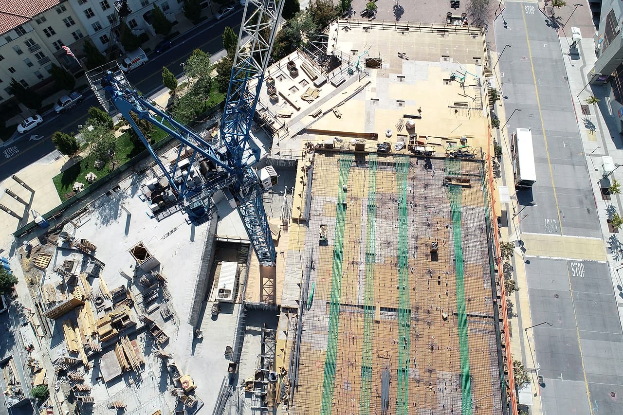 Looking straight down on a mid-rise building site: a tower crane, a reinforced deck ready for concrete, stored materials and the street beside it.