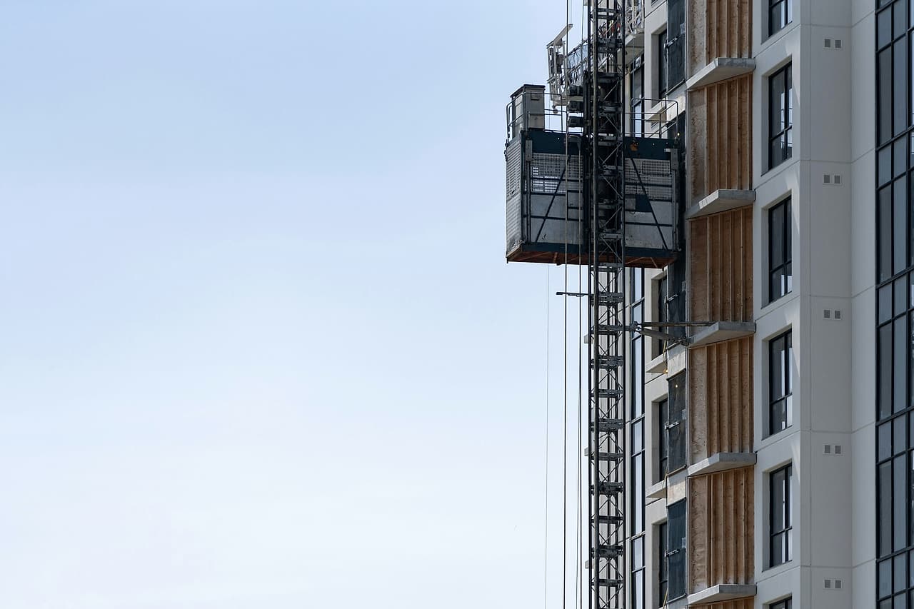 A construction hoist stands beside an unfinished building facade.