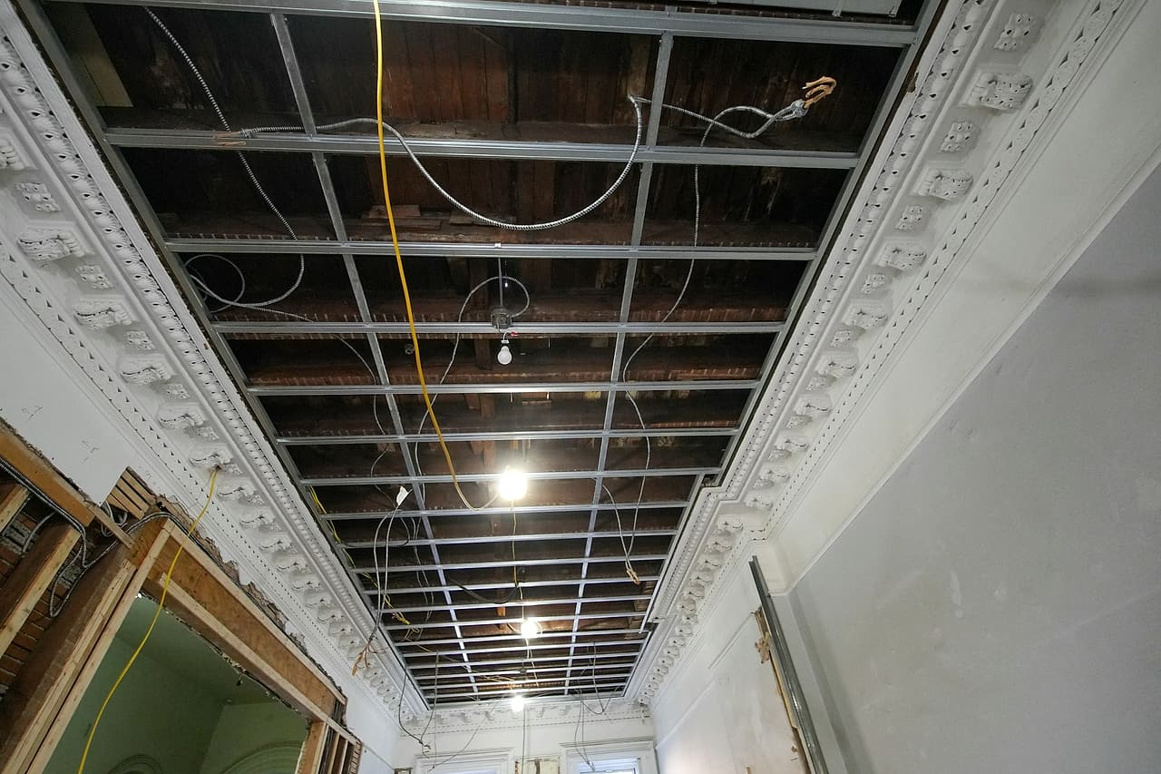 An old building's ceiling opened up during renovation, with a new metal grid, loose armoured cable and work lights hanging.