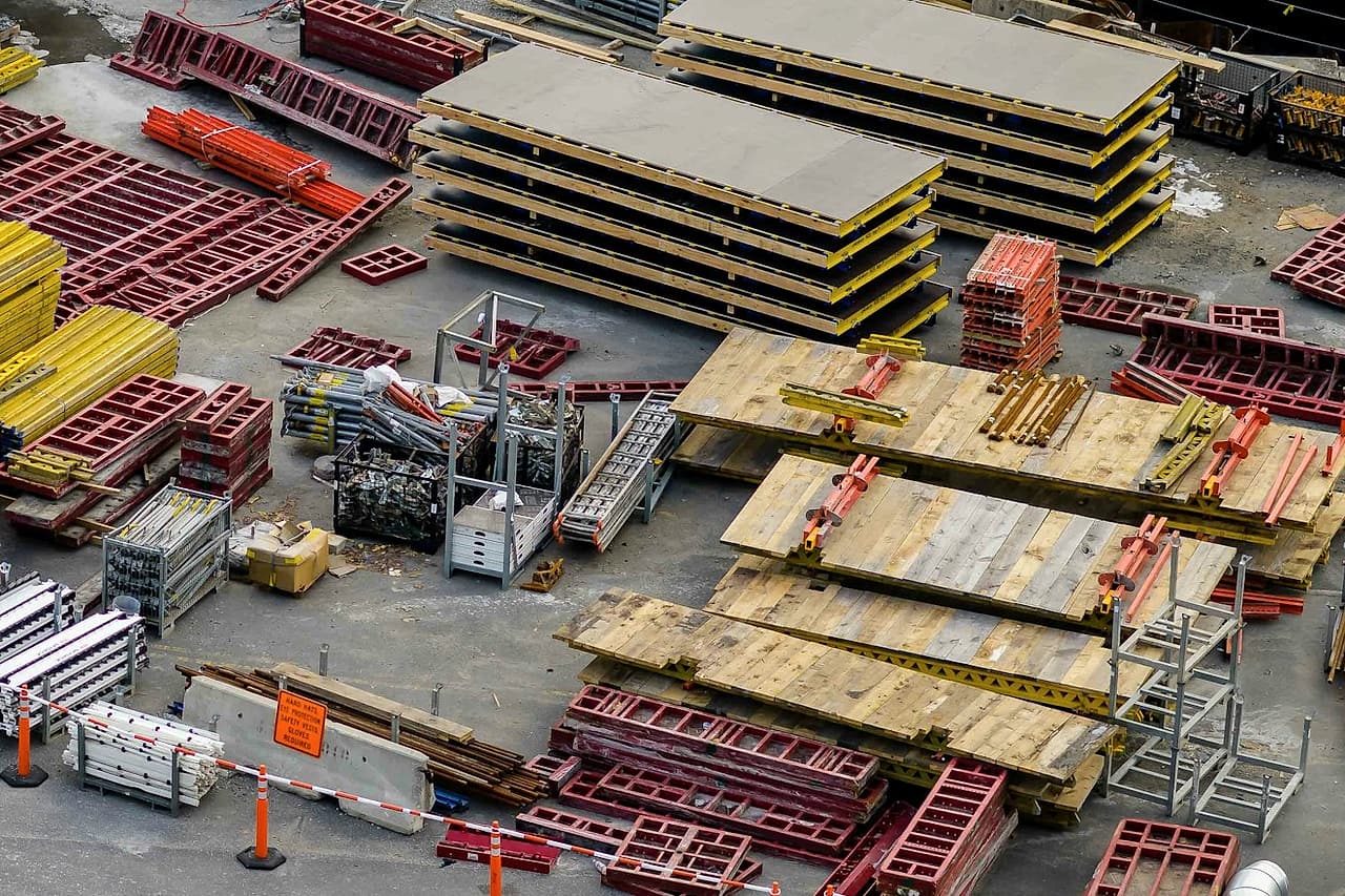 Formwork panels, beams and frames are organized in separate stacks in a site staging area.