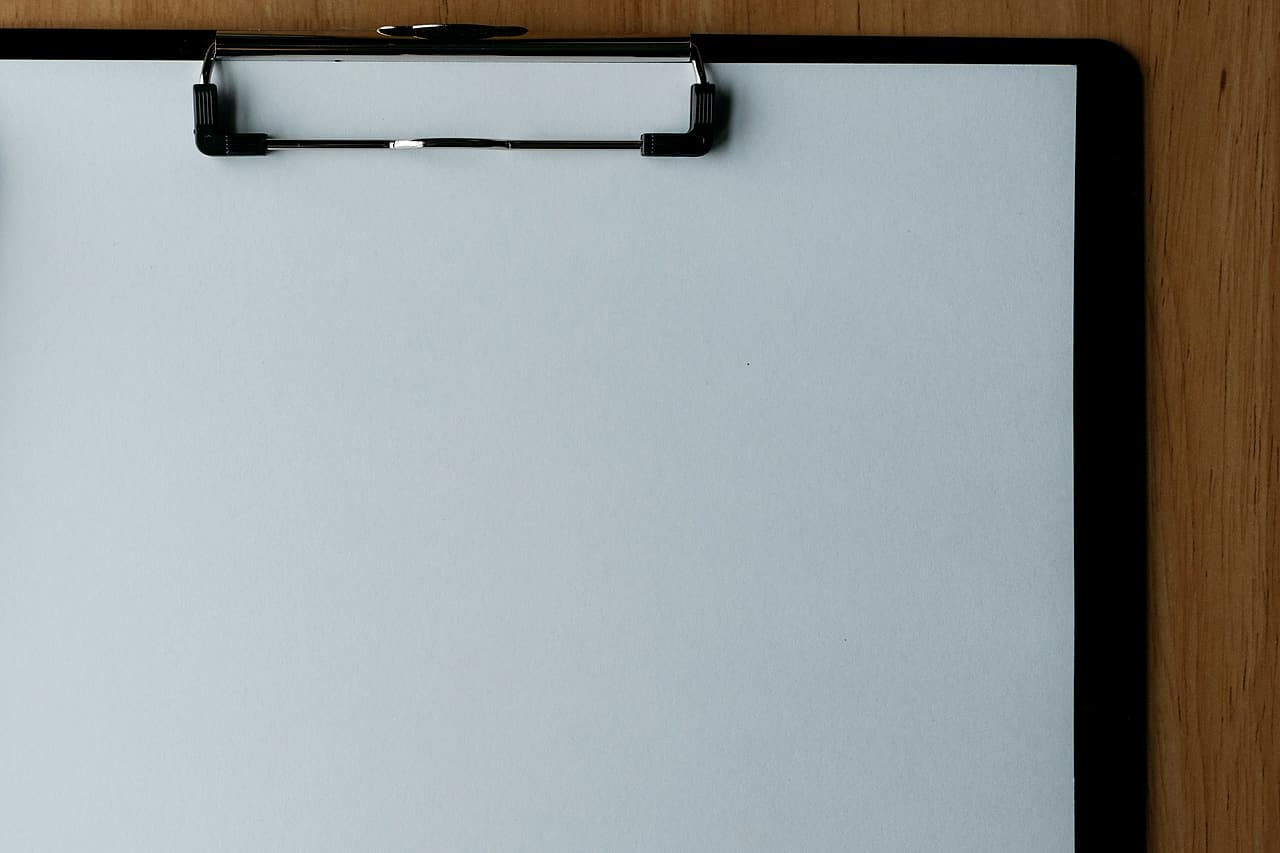 Blank paper rests on a black clipboard on a wooden desk.