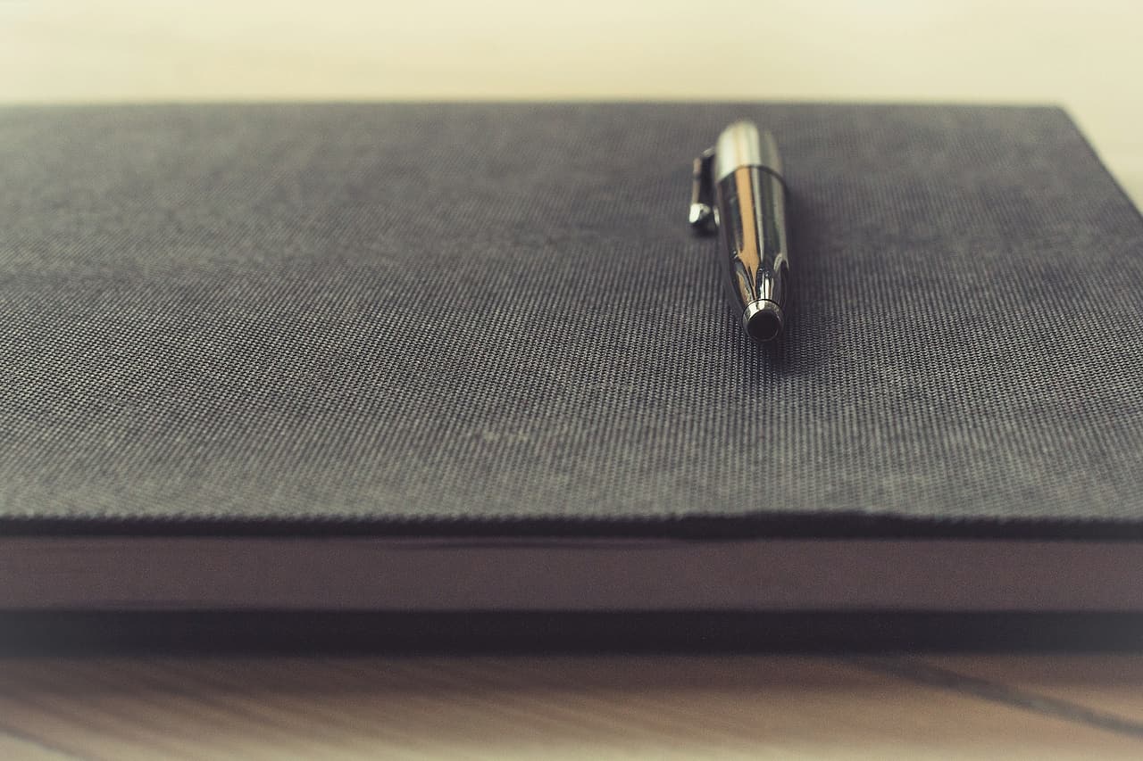 A pen rests on a closed textured notebook.