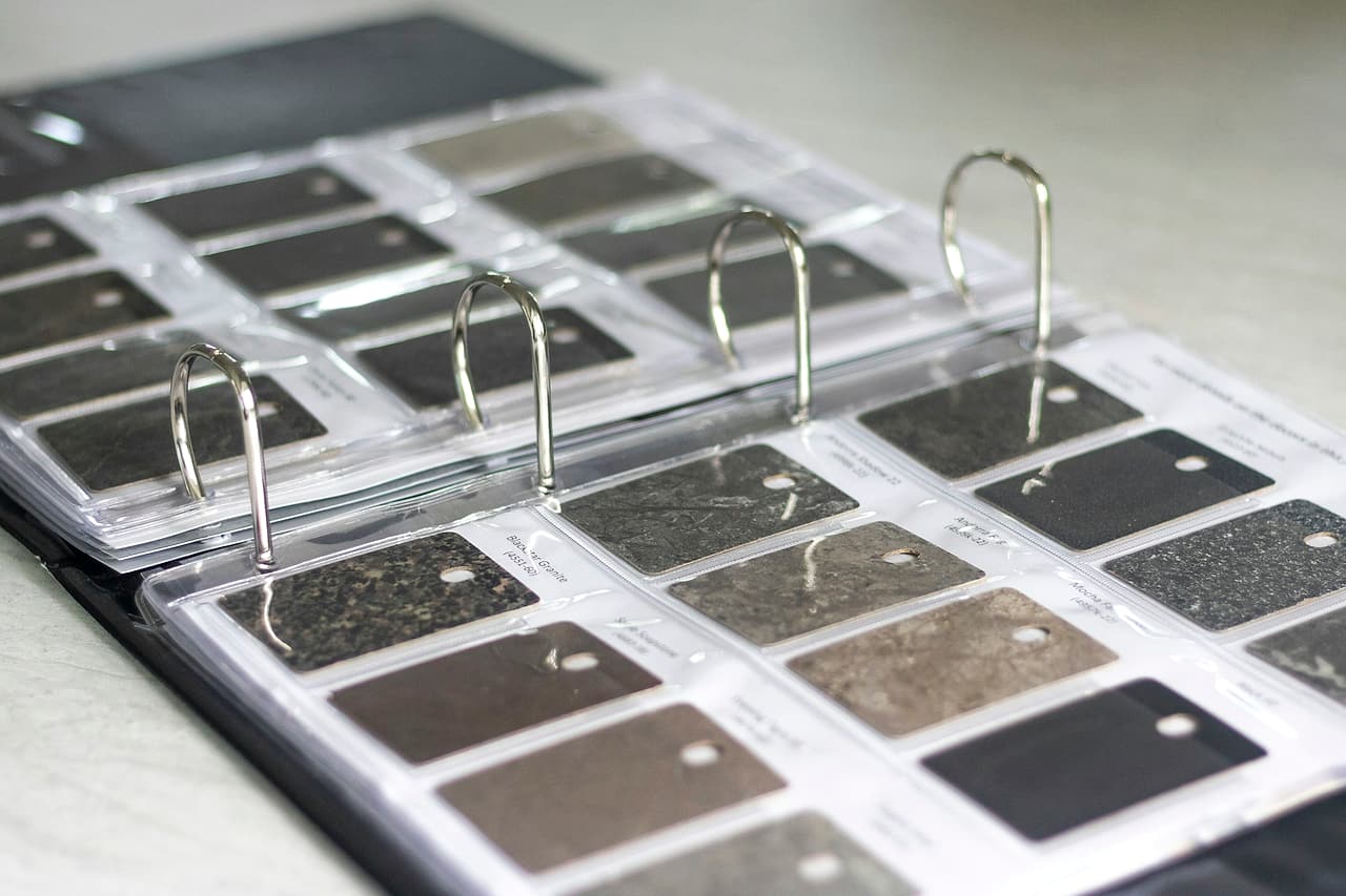 An open ring binder of laminate and stone sample chips in clear sleeves, each labelled, on a pale desk.