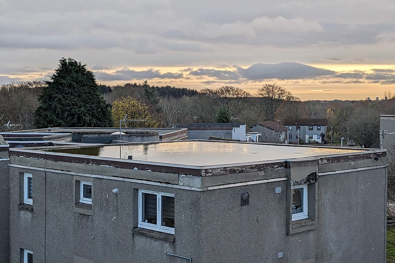 Standing water covers part of an unoccupied flat roof above a residential building.