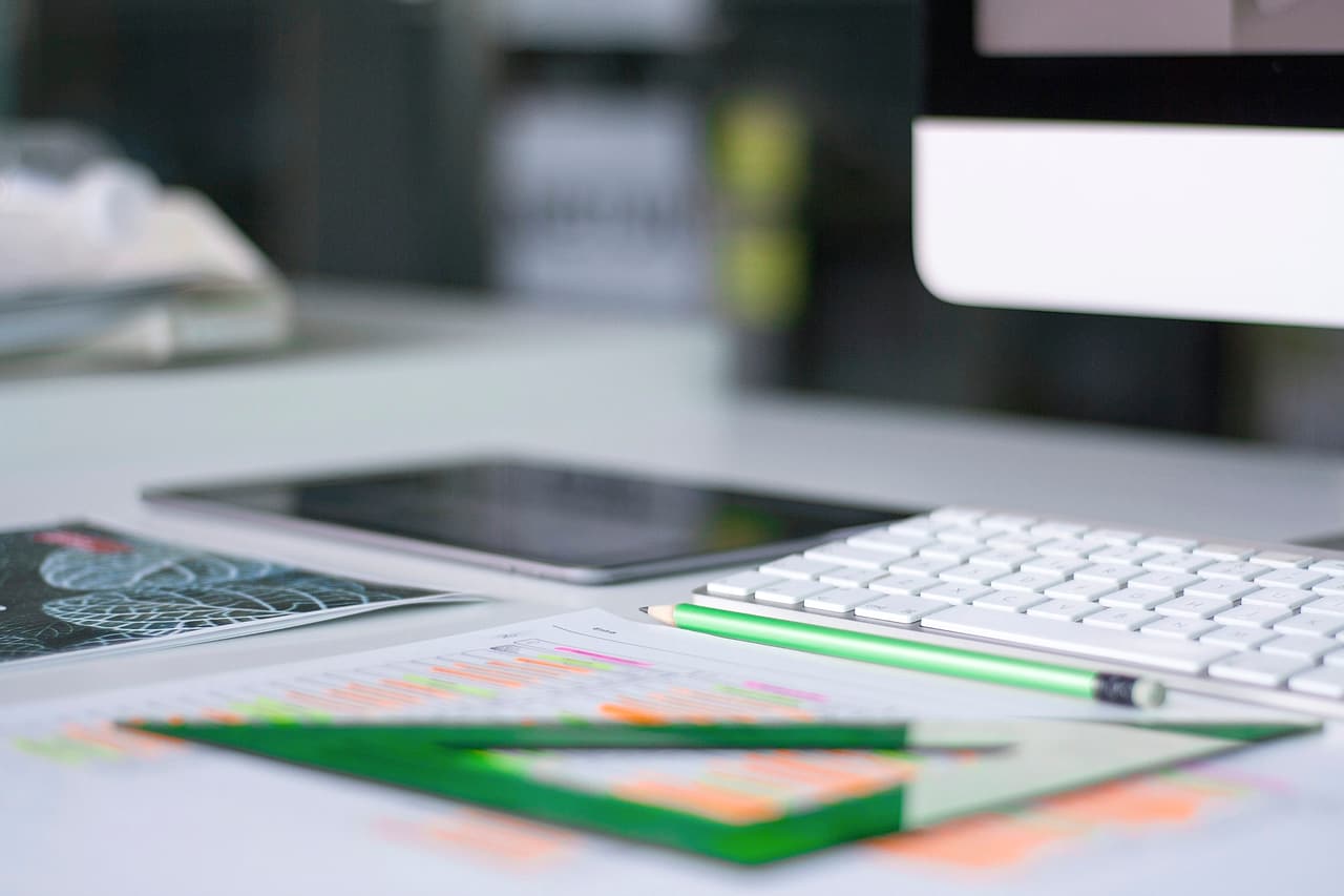 Marked drawings, pencils and a green drawing triangle lie beside a keyboard on an office desk.