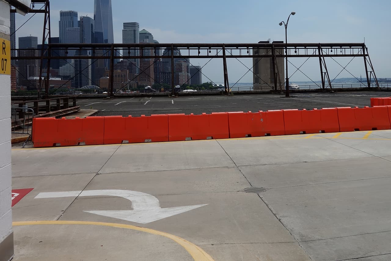An unoccupied concrete parking deck has painted lane markings and orange barriers beside a metal perimeter railing.
