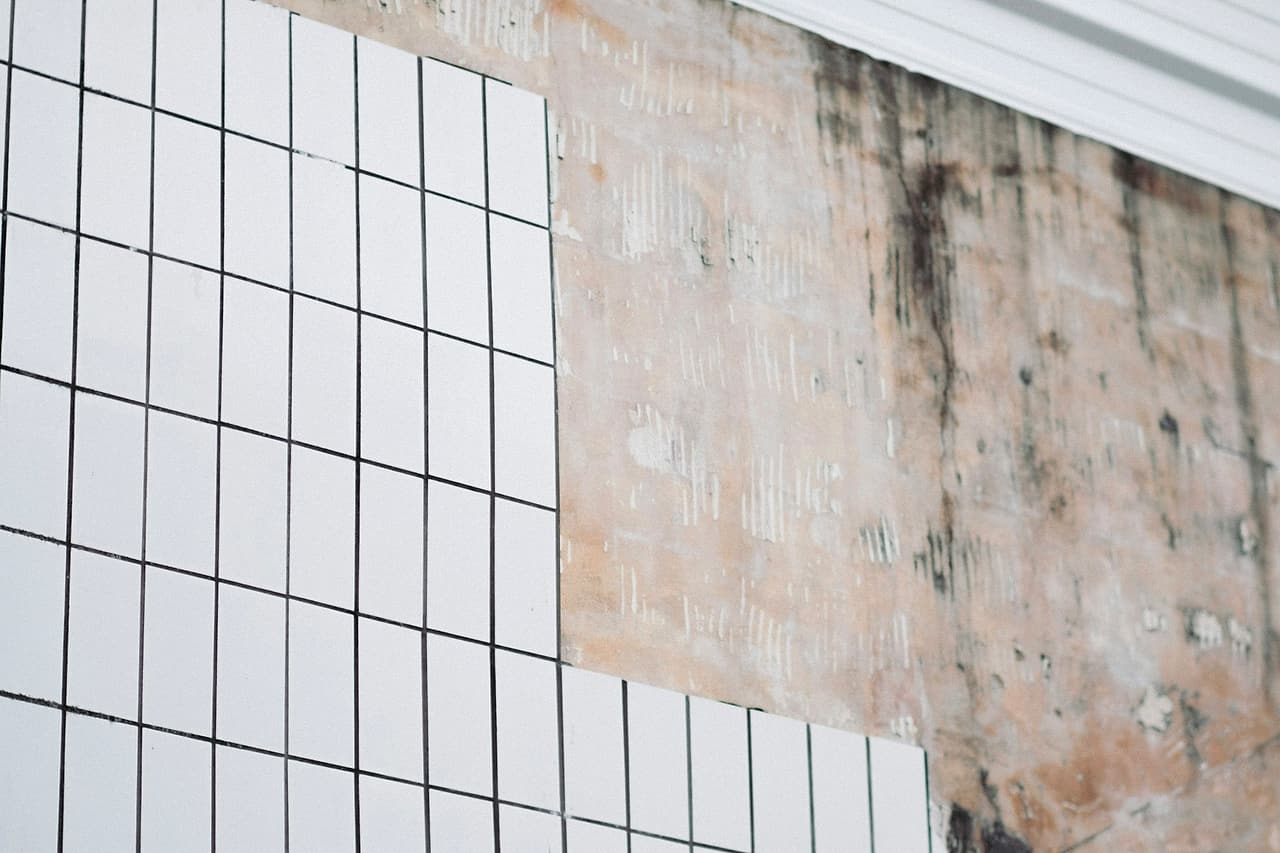 Tiles have been removed from part of an empty room's wall.