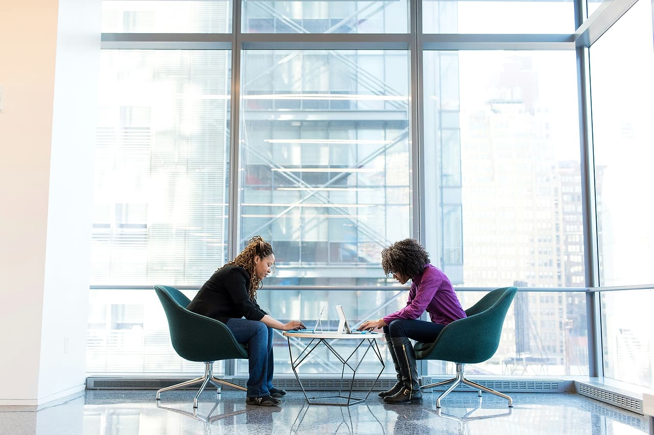 Two colleagues use laptops during a quiet office discussion.