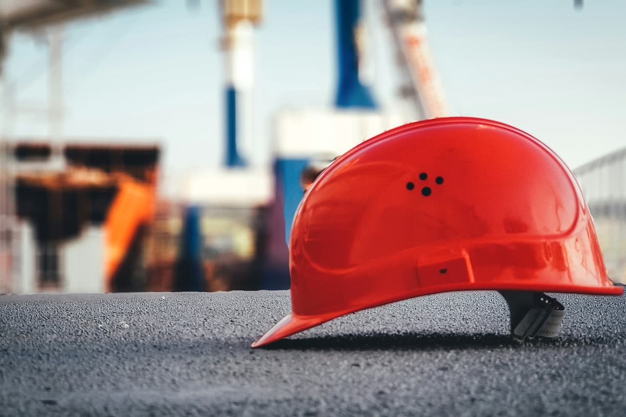 A red hard hat rests on a concrete surface with an unfinished building behind it.