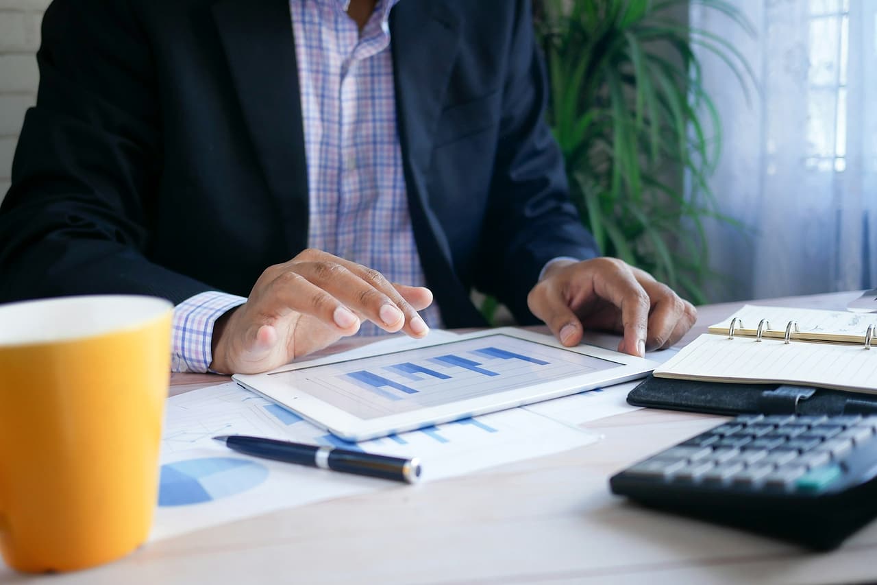 Hands review a chart on a tablet beside printed graphs, a calculator and an open notebook.